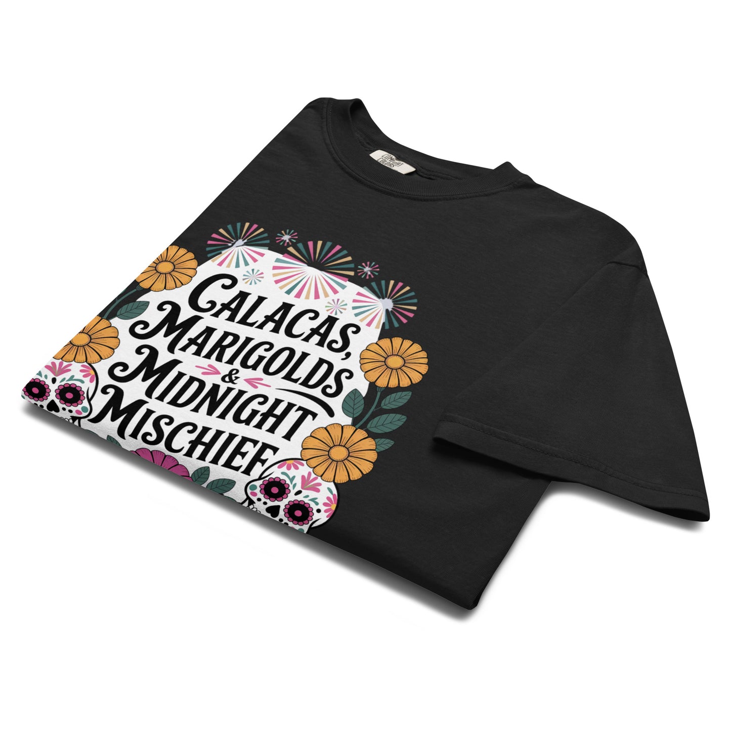 Folded black t-shirt with bold Día de los Muertos artwork of sugar skulls, marigolds, and festive typography reading ‘Calacas, Marigolds & Midnight Mischief.’