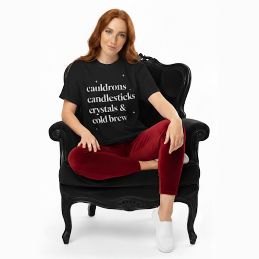 Model wearing a black t-shirt printed with the phrase ‘cauldrons, candlesticks, crystals & cold brew,’ styled with a witchy minimalist aesthetic.