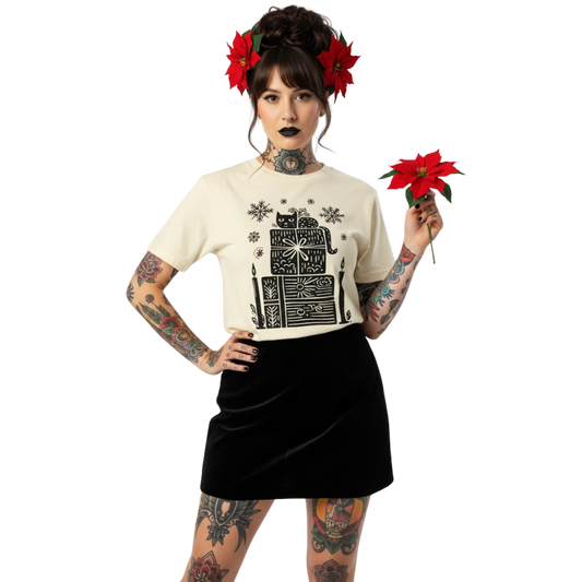 Woman wearing ivory witchy holiday T-shirt featuring candle and gift stack design, styled with black skirt and poinsettia bouquet.