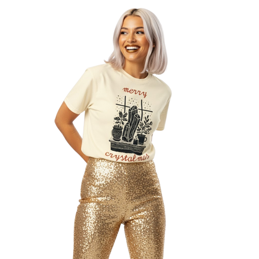 Woman wearing ivory “Merry Crystalmas” T-shirt with crystal and candle design, styled with gold sequin pants and cheerful holiday look.