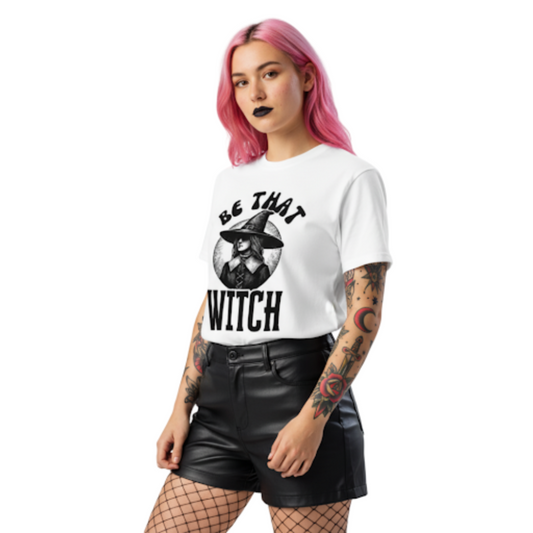 Model wearing a white t-shirt printed with a vintage witch in a wide hat and the phrase ‘Be That Witch’; witchy dark-feminine aesthetic.