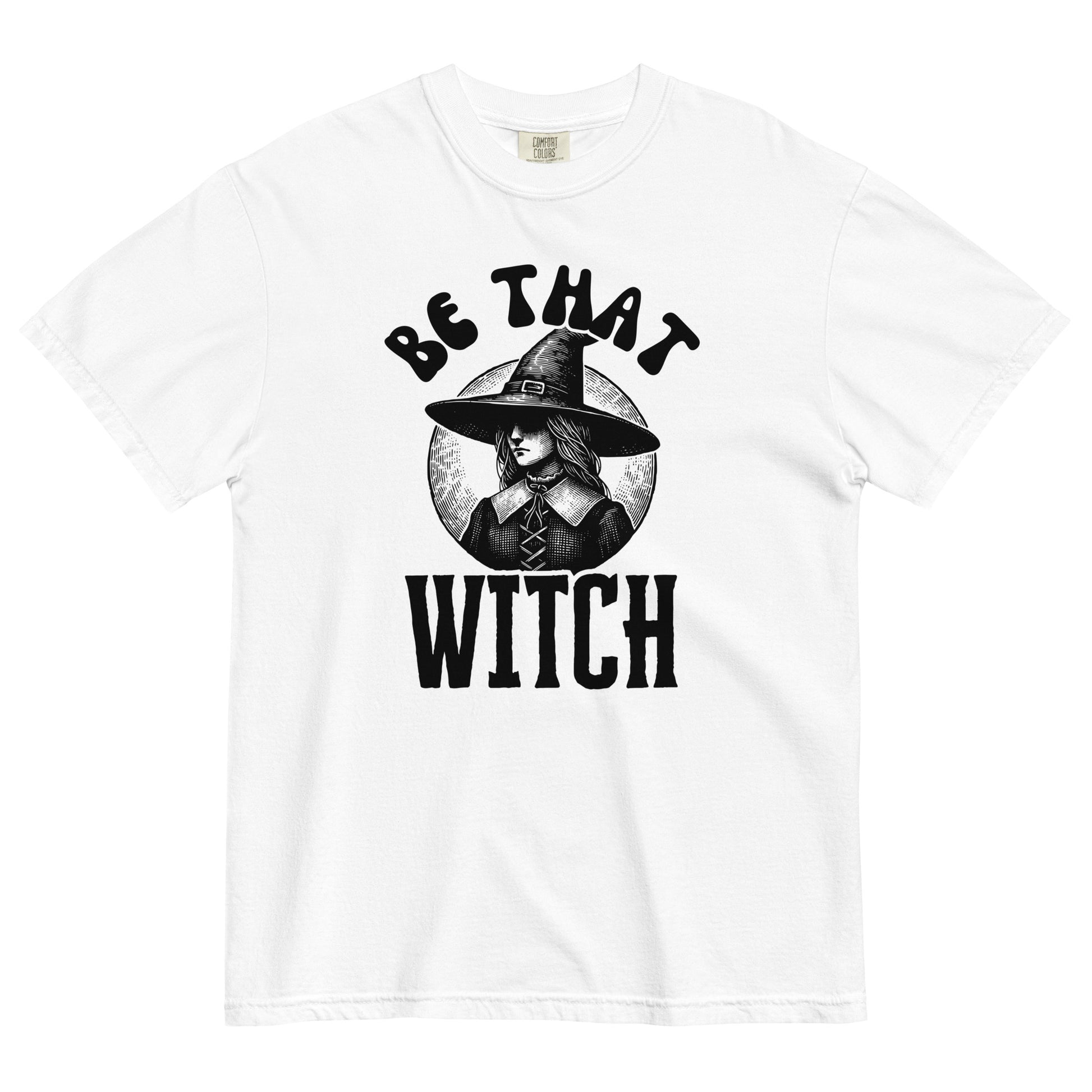White t-shirt featuring a vintage-style witch in a wide hat with the phrase ‘Be That Witch’ in bold black lettering.