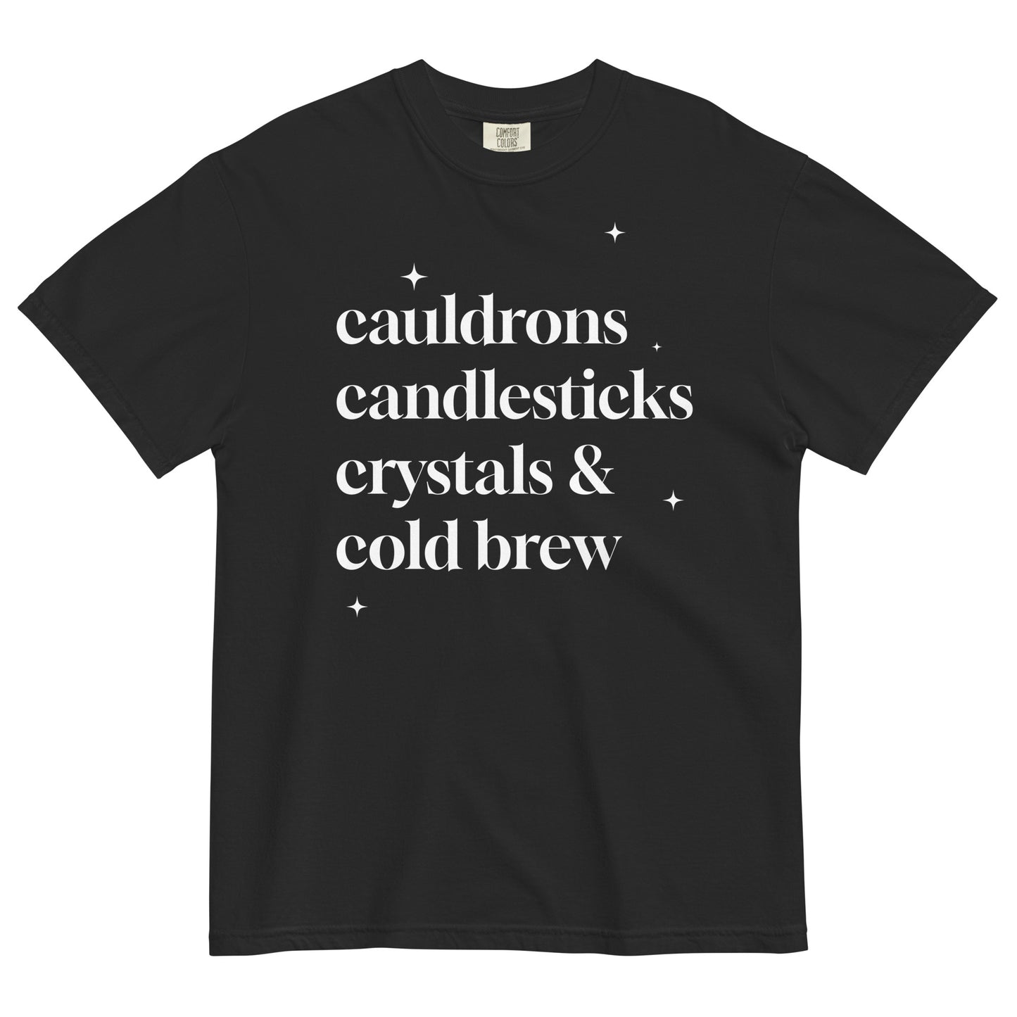 Black t-shirt laid flat with white serif text reading ‘cauldrons, candlesticks, crystals & cold brew’ surrounded by small star accents.