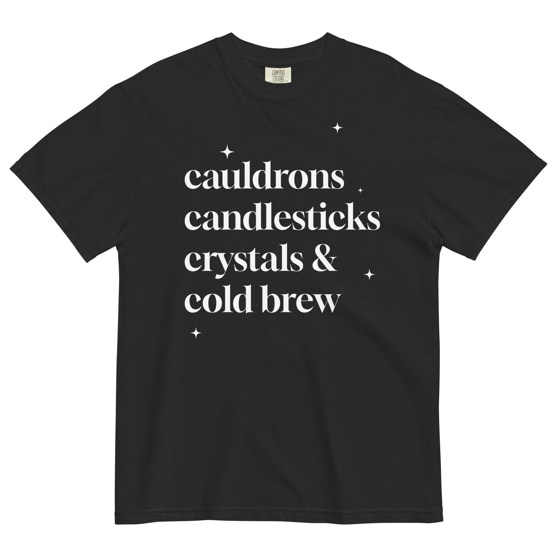 Black t-shirt laid flat with white serif text reading ‘cauldrons, candlesticks, crystals & cold brew’ surrounded by small star accents.