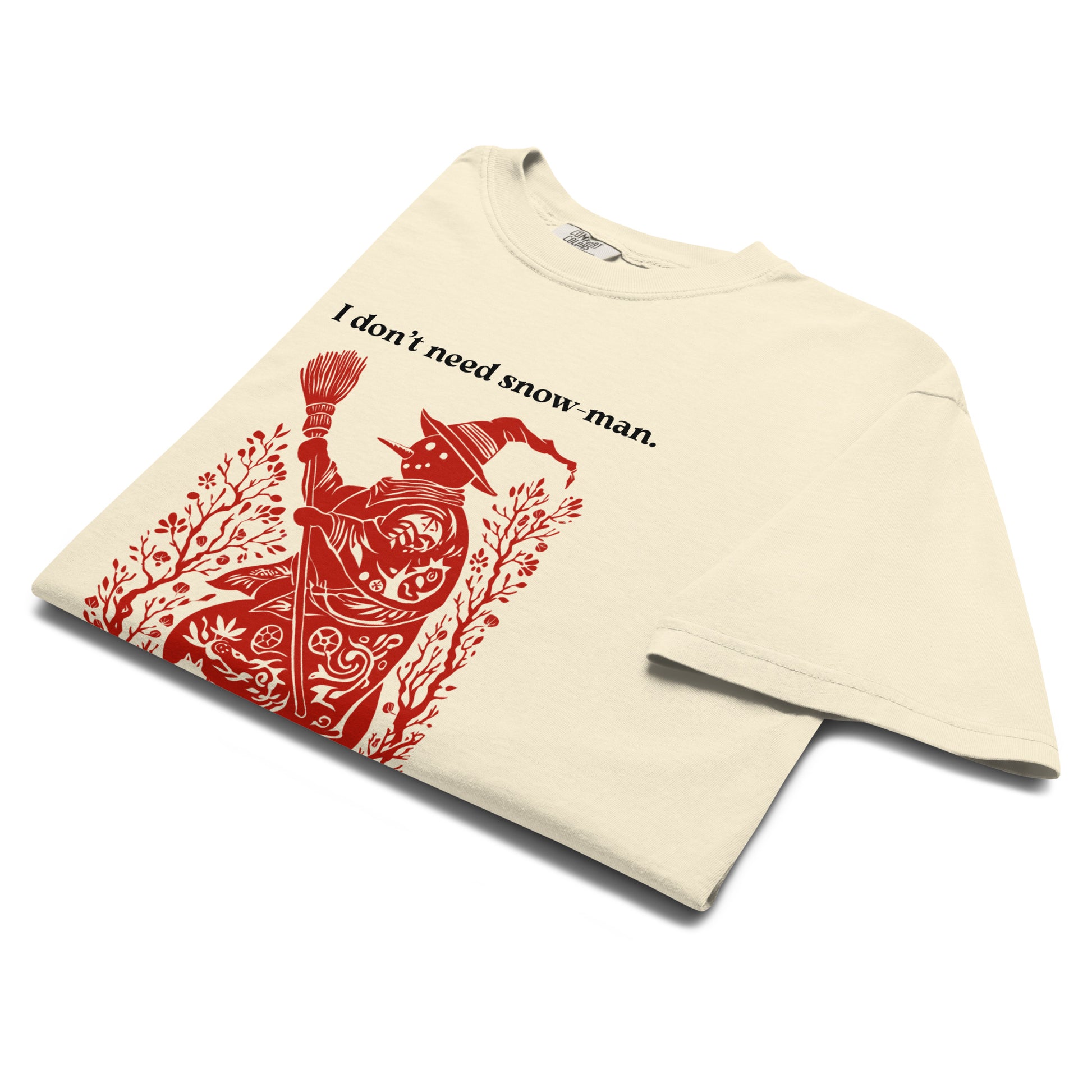 Folded lay-flat view of cream “I don’t need snow man” T-shirt showing bold red witch illustration print.