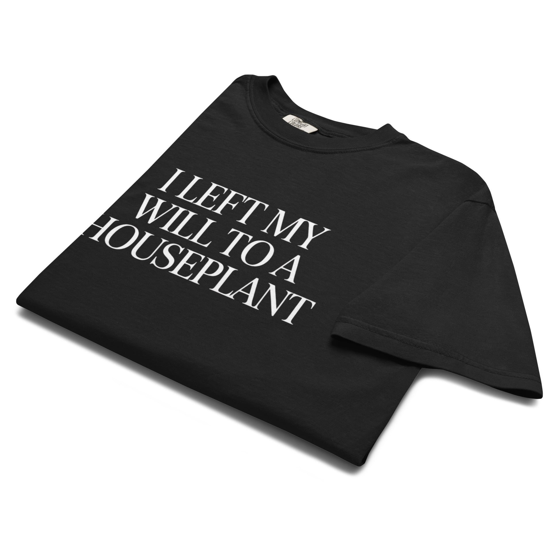 Folded black “I Left My Will to a Houseplant” t-shirt flat lay with minimalist typography, perfect for fans of dark humor and plant parent energy.