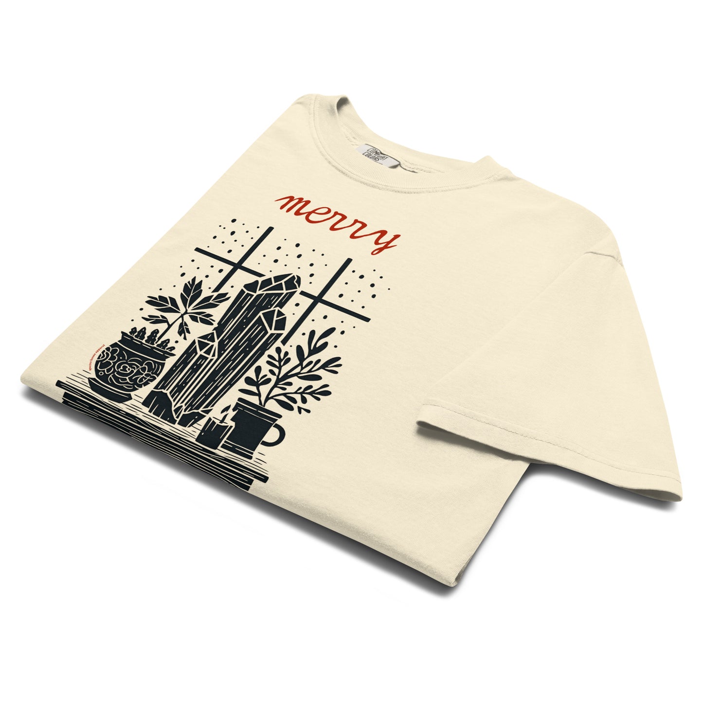 Folded lay-flat view of ivory “Merry Crystalmas” T-shirt showing black and red festive crystal illustration.