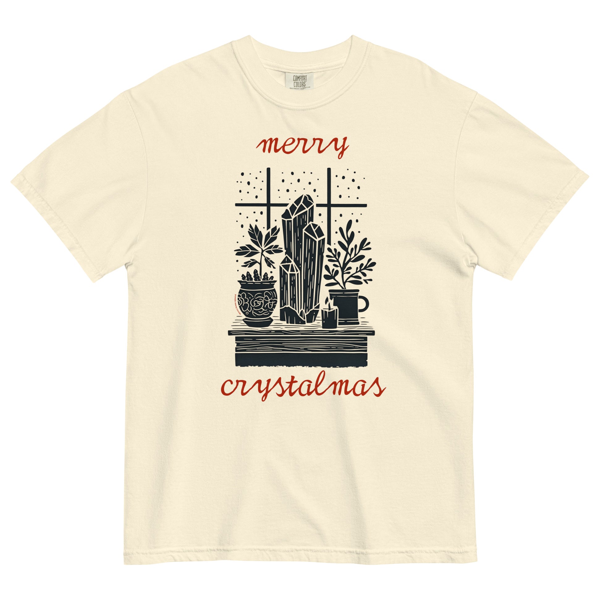 Ivory Comfort Colors T-shirt with “Merry Crystalmas” design featuring crystals, candles, and plants, shown lay flat on white background.