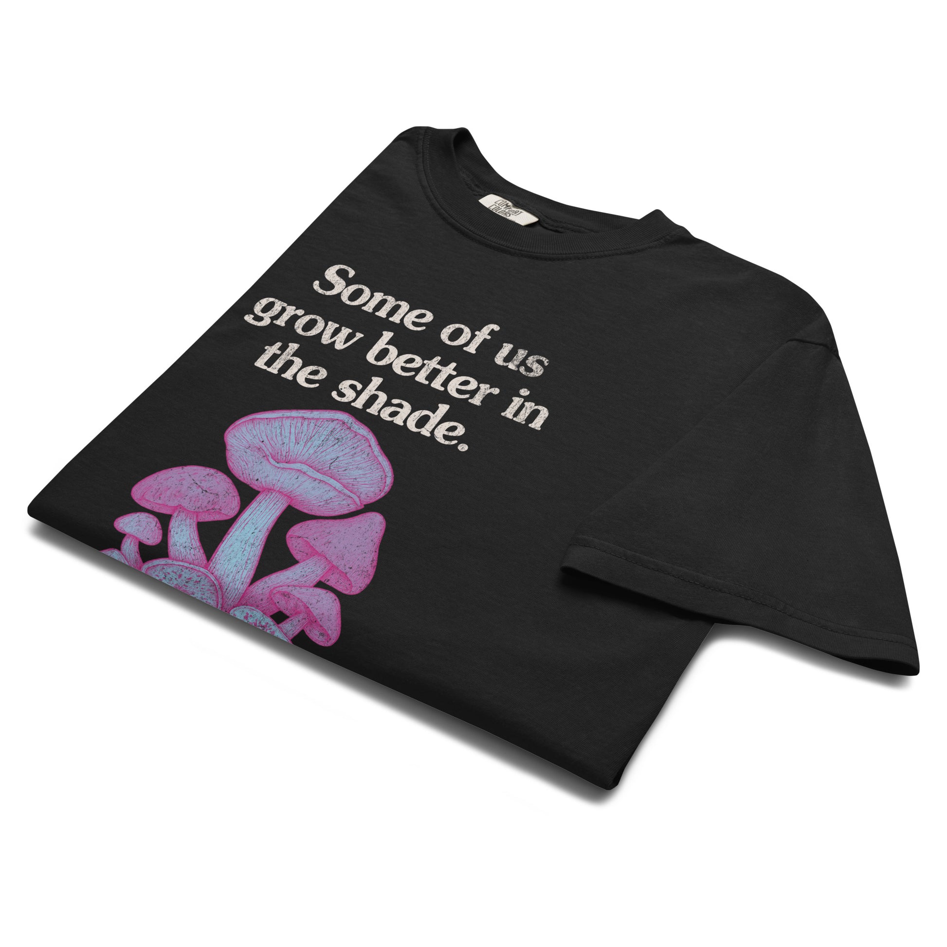 Folded black “Some of us grow better in the shade” t-shirt flat lay with pastel mushroom illustration, perfect for lovers of soft dark academia and forestcore style.
