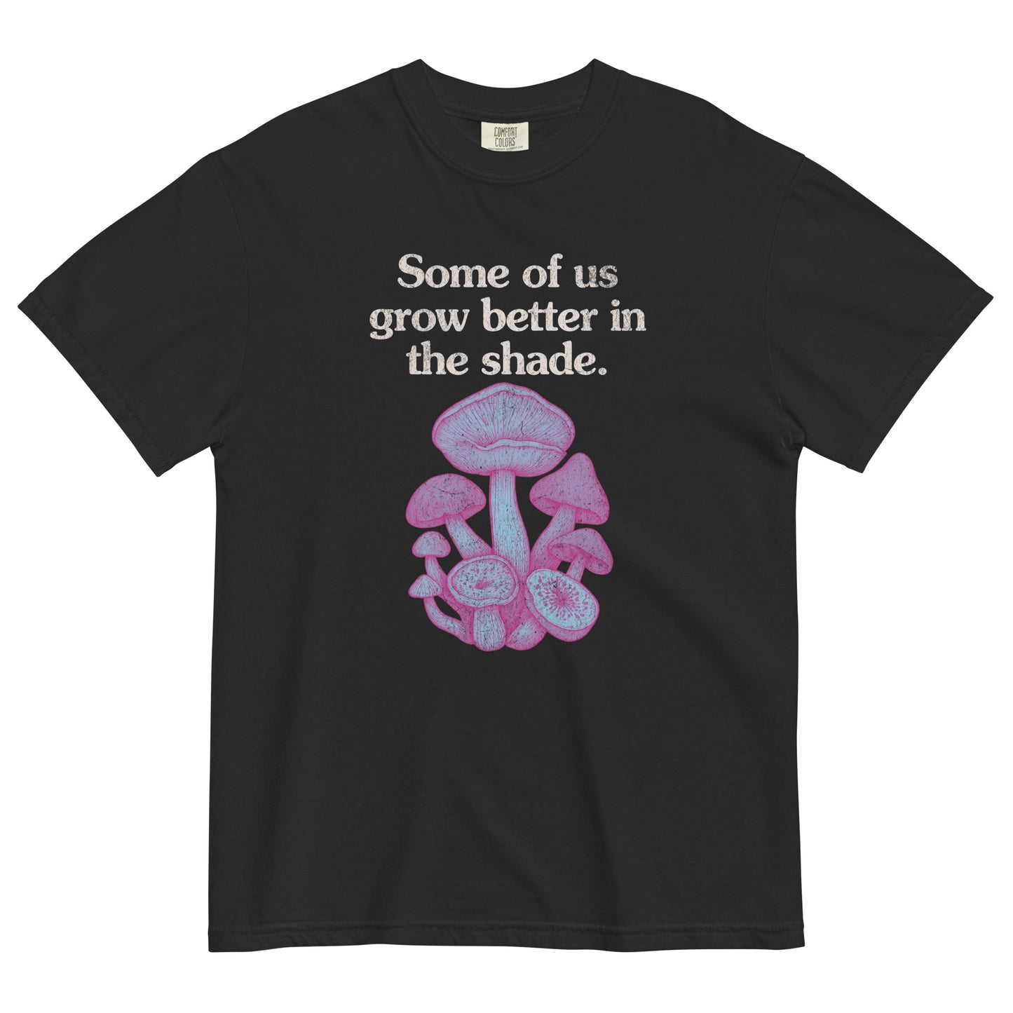 Black t-shirt lay flat with text reading “Some of us grow better in the shade” above a cluster of pink and purple mushrooms, a dreamy gothic botanical tee.