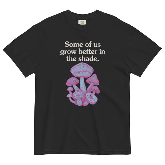 Black t-shirt lay flat with text reading “Some of us grow better in the shade” above a cluster of pink and purple mushrooms, a dreamy gothic botanical tee.
