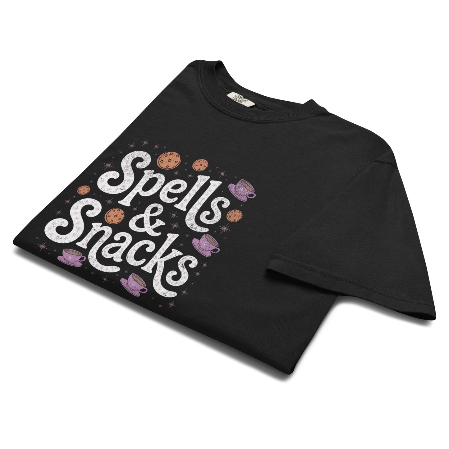 Folded black “Spells & Snacks” t-shirt flat lay showing playful witchy lettering and illustrated treats, perfect for soft goths and magical food lovers alike.