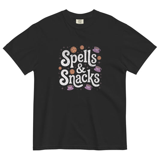 Black t-shirt lay flat featuring white “Spells & Snacks” text surrounded by pastel cookies, stars, and potion bottles — a cute witchy cottagecore graphic tee.