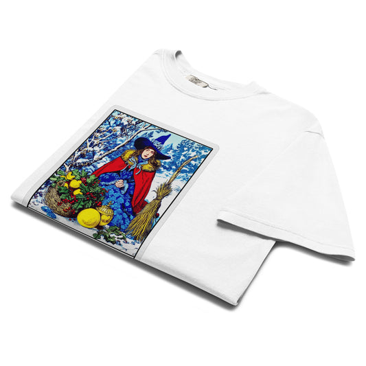 Folded lay-flat view of white “The Winter Witch” T-shirt showing vibrant tarot-style illustration with winter witch, broom, and citrus details.