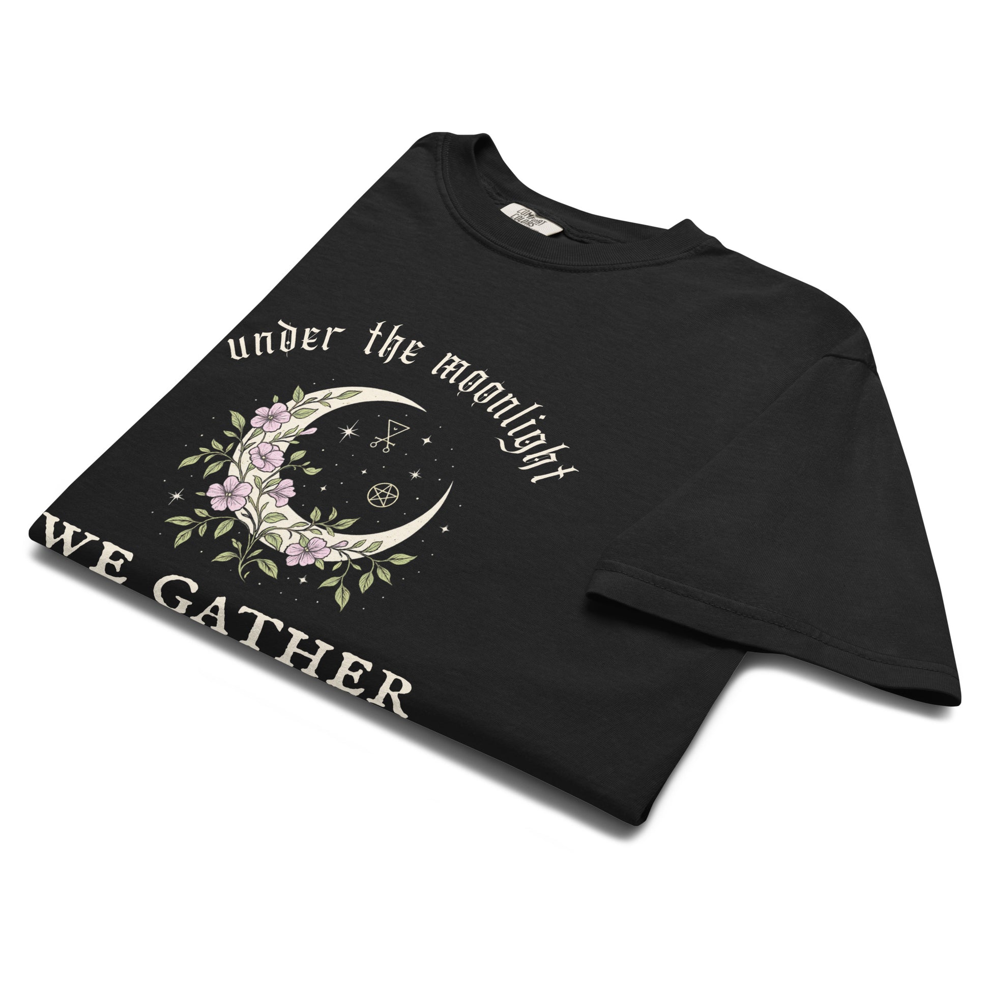 Flat lay of “Under the Moonlight We Gather” folded t-shirt featuring a crescent moon surrounded by lilac flowers, perfect for boho, witchy, or dark academia styles.