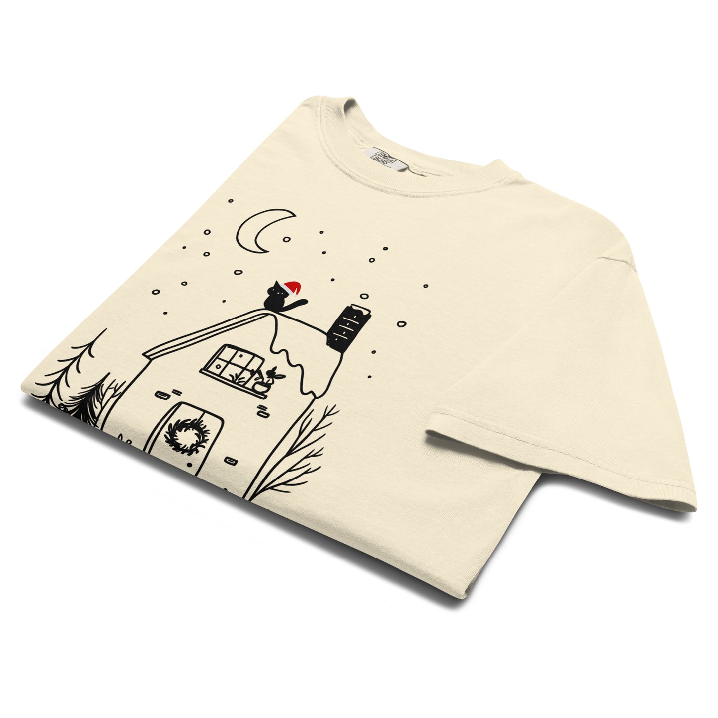 Folded lay-flat view of ivory witchy cottage holiday T-shirt showing detailed moon, snow, and cozy cabin illustration.