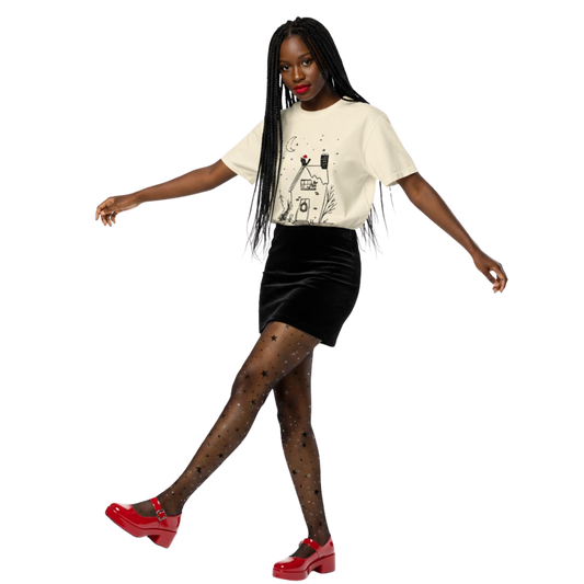 Woman wearing ivory witchy cottage holiday T-shirt with moon and wreath design, styled with black skirt and red heels.